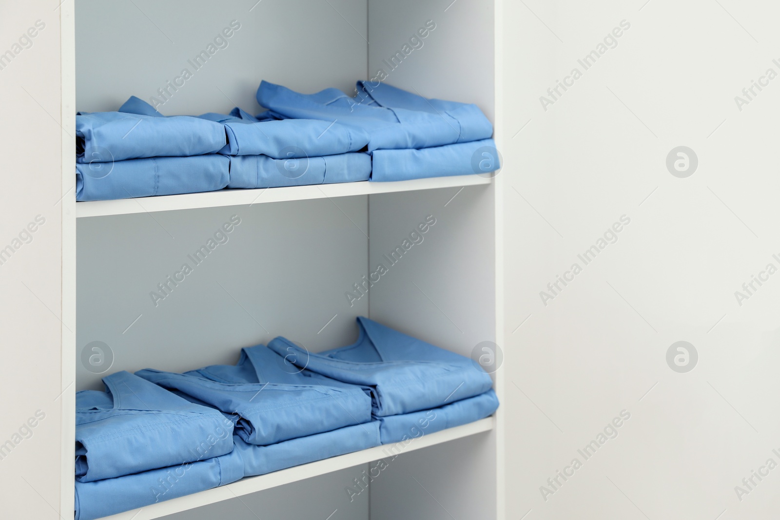 Photo of Light blue medical uniforms on white rack indoors, space for text
