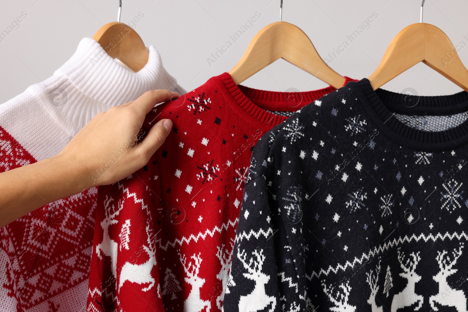 Photo of Woman choosing Christmas sweater from rack near light wall, closeup