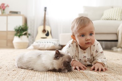 Cute little baby with adorable cat on floor at home