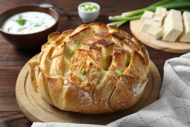 Photo of Freshly baked bread with tofu cheese, green onions and sauce on wooden table