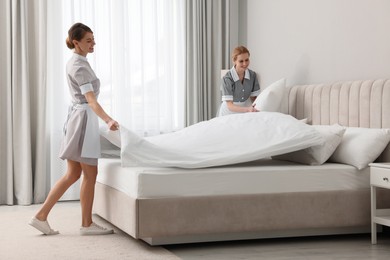 Professional chambermaids making bed in hotel room