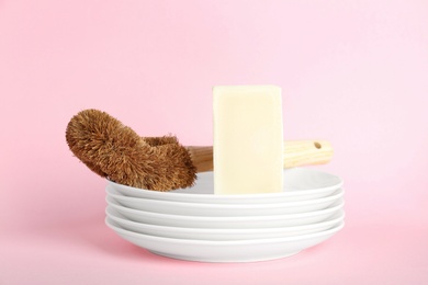 Cleaning supplies for dish washing and plates on pink background