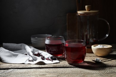 Photo of Delicious hibiscus tea in cups, sugar cubes and dry roselle petals on wooden table