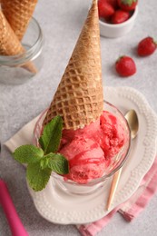 Delicious scoops of strawberry ice cream with mint and wafer cone in glass dessert bowl served on grey table, above view