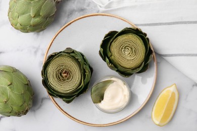 Photo of Delicious cooked artichokes with tasty sauce served on white marble table, flat lay