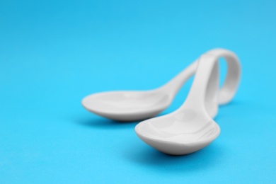 Photo of Clean empty ceramic appetizer spoons on blue background, space for text