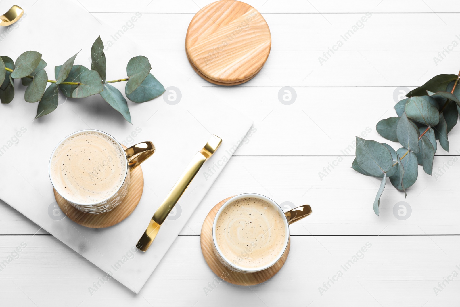 Photo of Mugs of coffee with stylish cup coasters and eucalyptus branches on white wooden table, flat lay