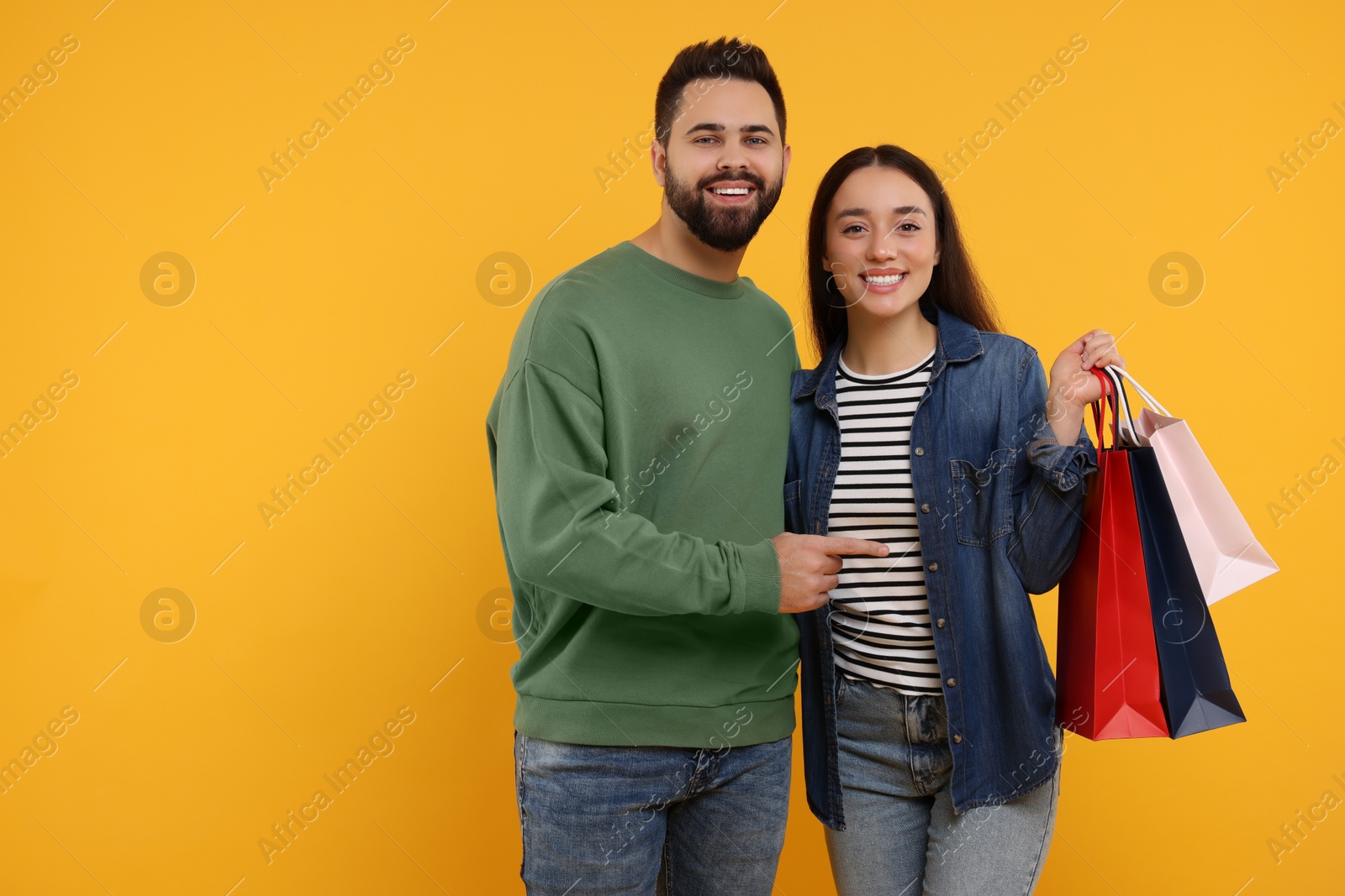 Photo of Happy couple with shopping bags on orange background. Space for text