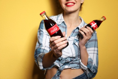 Photo of MYKOLAIV, UKRAINE - NOVEMBER 28, 2018: Young woman with bottles of Coca-Cola on color background, closeup