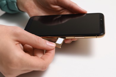 Woman putting SIM card tray in smartphone at white table, closeup