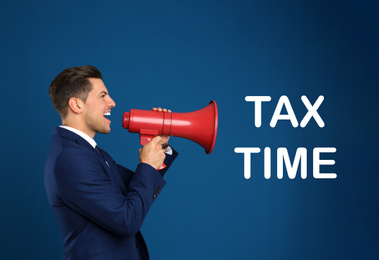 Handsome man with megaphone and text TAX TIME on blue background