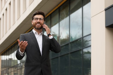 Photo of Handsome businessman talking on smartphone while walking outdoors, space for text