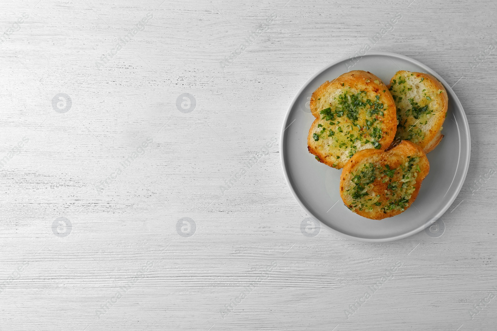 Photo of Slices of toasted bread with garlic and herbs on white wooden table, top view. Space for text