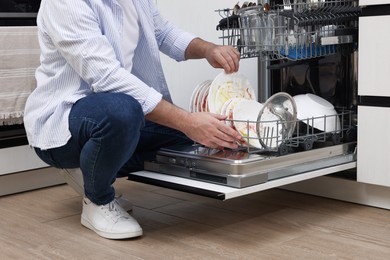 Photo of Man loading dishwasher with dirty plates indoors, closeup