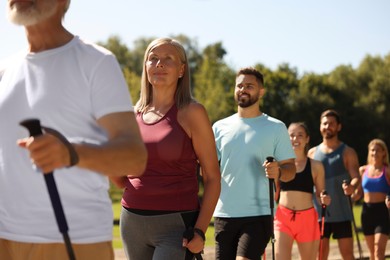 Photo of Group of people practicing Nordic walking with poles outdoors on sunny day