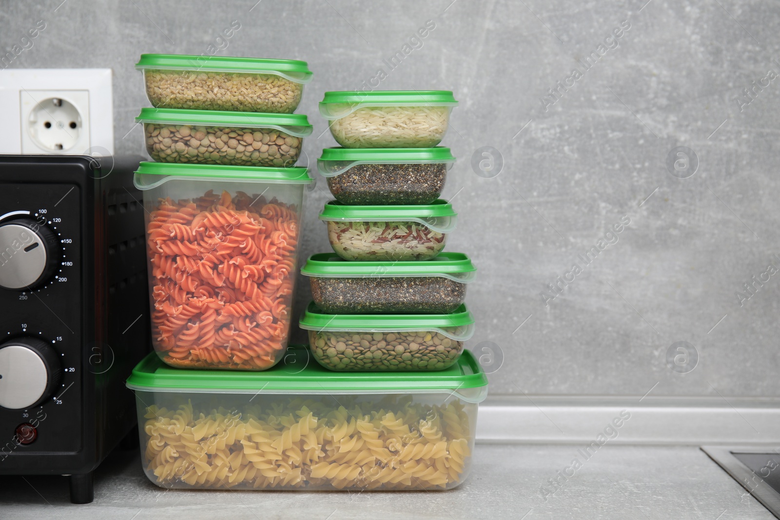 Photo of Plastic containers filled with food products on grey table in kitchen. Space for text