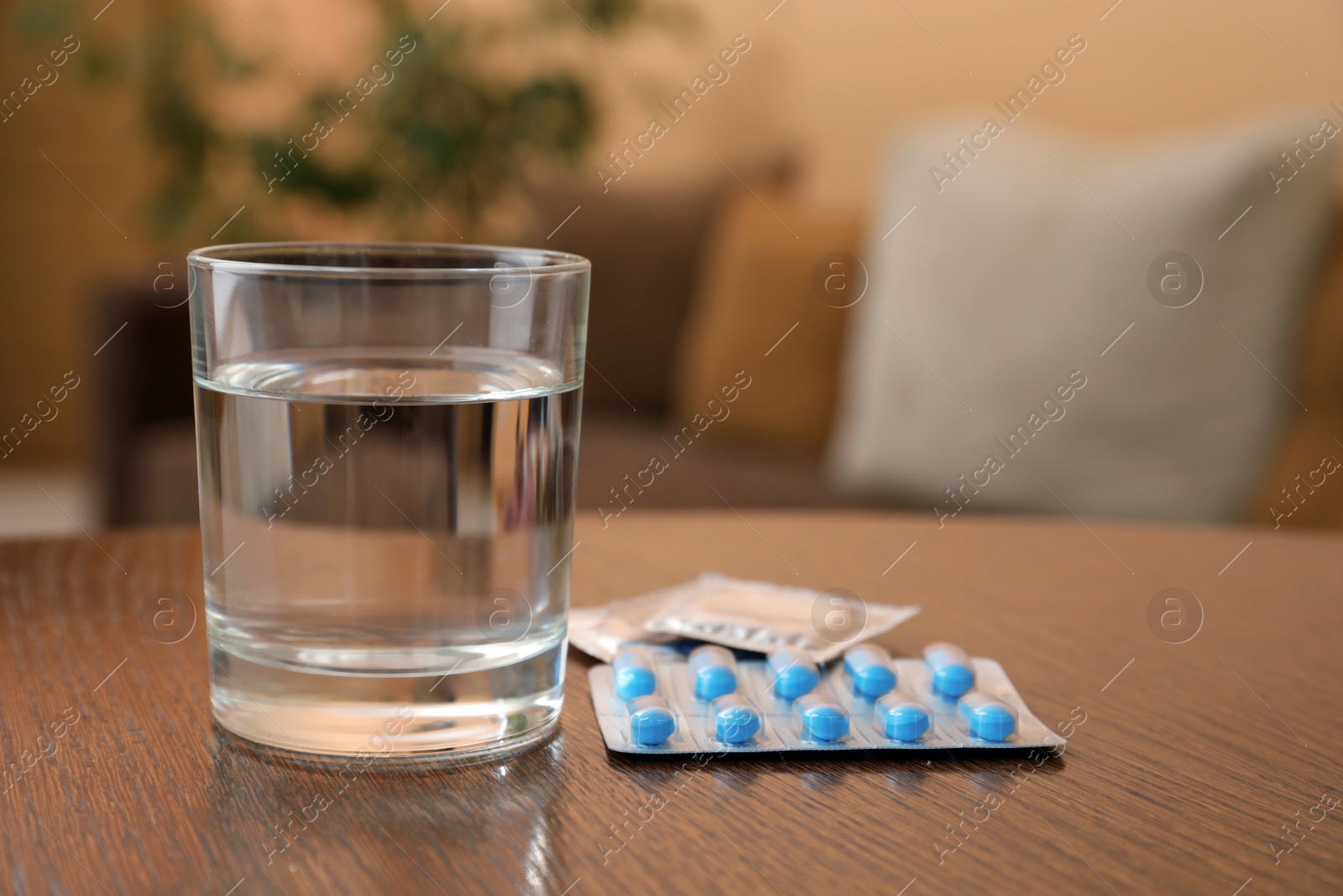 Photo of Glass of water, condoms and pills on wooden table indoors, space for text. Potency problem concept