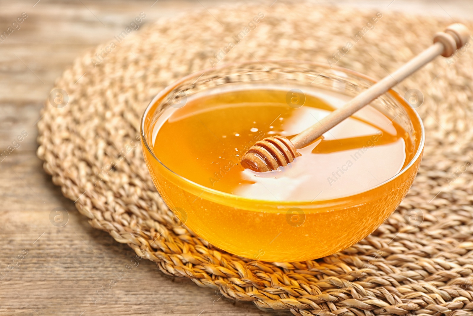 Photo of Tasty honey in glass bowl on wooden table, closeup