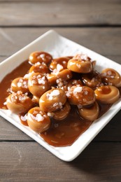 Photo of Plate with tasty candies, caramel sauce and salt on wooden table