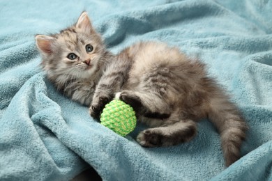 Photo of Cute kitten playing with ball on light blue blanket