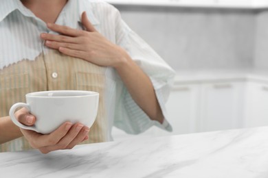 Photo of Woman with spilled coffee over her shirt at marble table in kitchen, closeup. Space for text