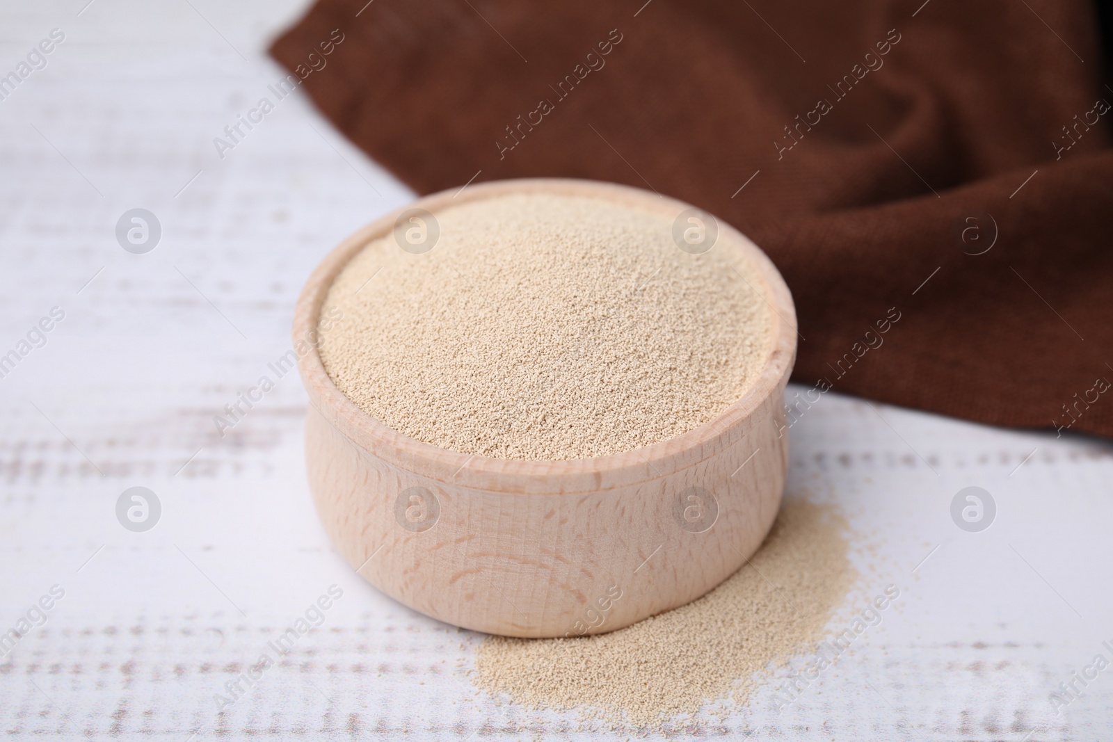 Photo of Granulated yeast in bowl on white wooden table, closeup