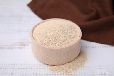 Granulated yeast in bowl on white wooden table, closeup