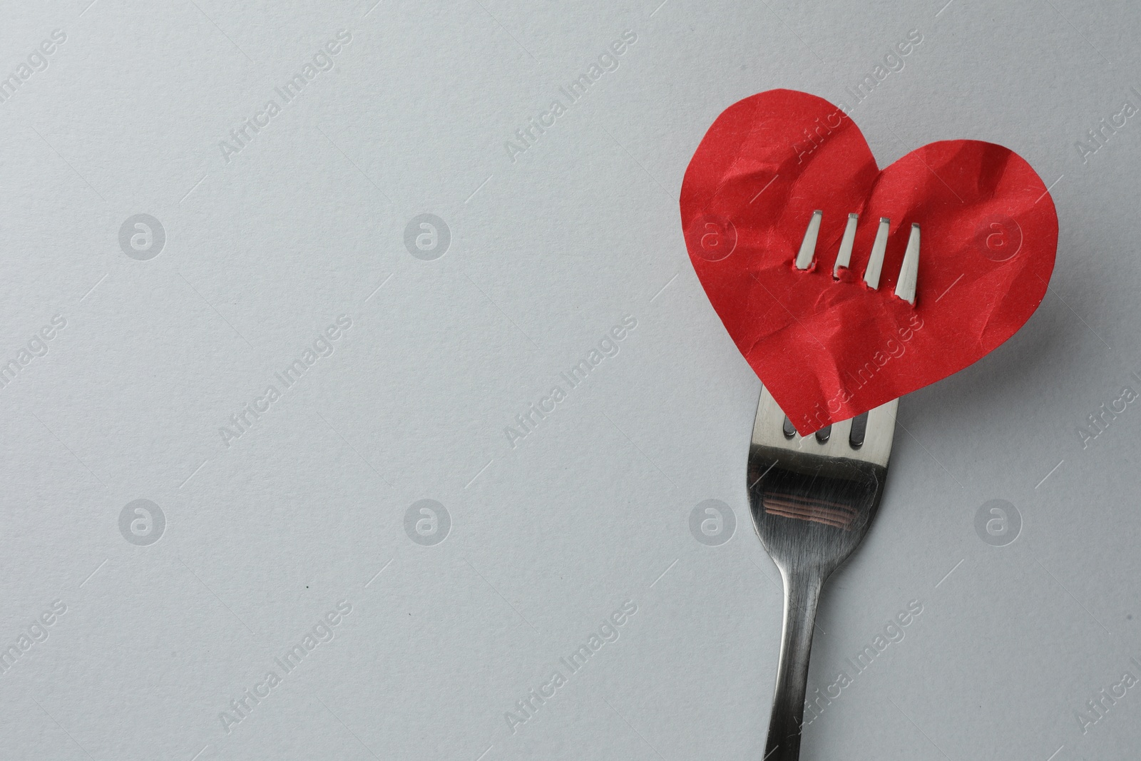 Photo of Broken heart. Red paper heart pierced with fork on white background, top view. Space for text