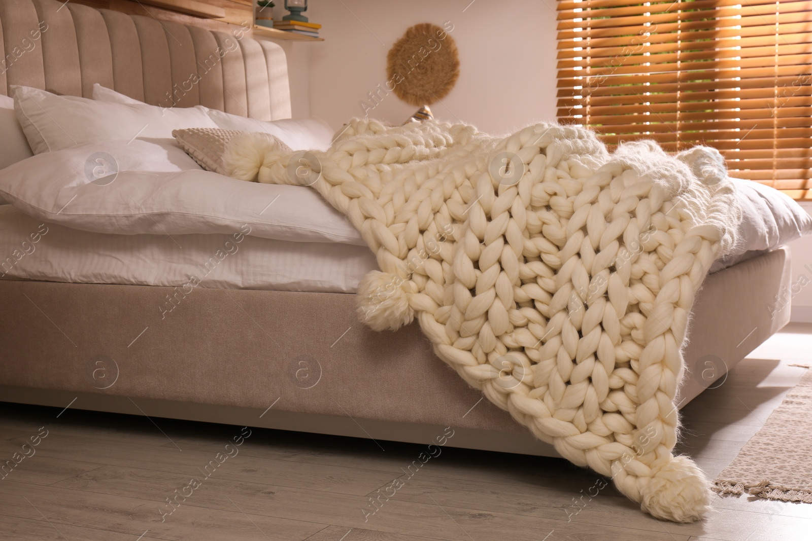 Photo of Bed with white knitted plaid indoors. Interior design