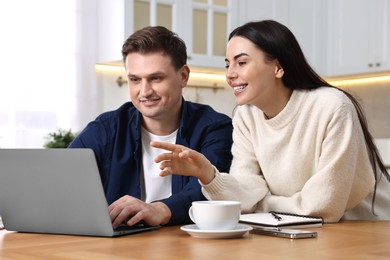 Photo of Happy couple using laptop together at wooden table in kitchen