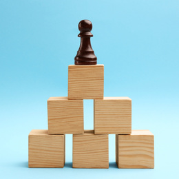 Photo of Black piece on top of wooden pyramid against light blue background. Career promotion concept