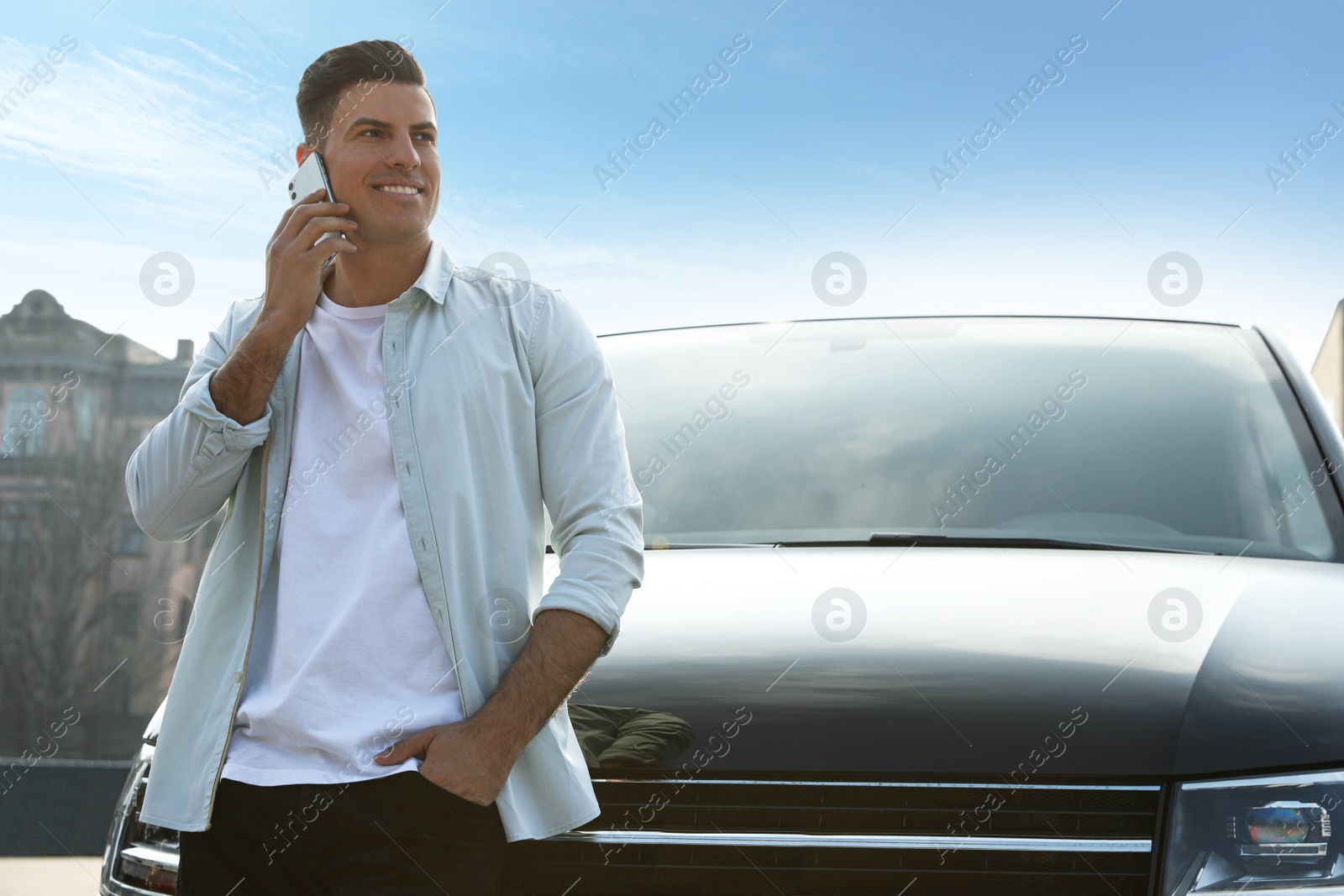 Photo of Handsome man talking on smartphone near modern car outdoors