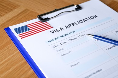 Photo of Visa application form for immigration to American flag and pen on table, closeup