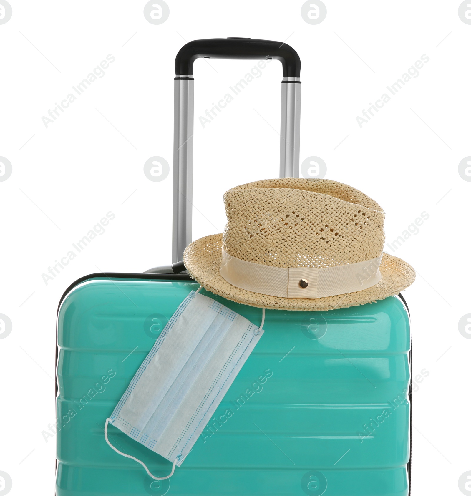 Photo of Stylish turquoise suitcase, hat and protective mask on white background. Travelling during coronavirus pandemic