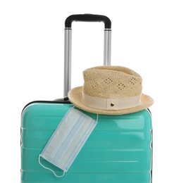 Stylish turquoise suitcase, hat and protective mask on white background. Travelling during coronavirus pandemic