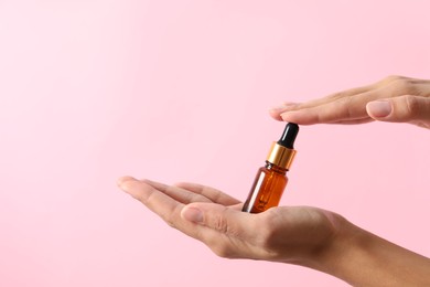 Photo of Woman with bottle of cosmetic serum on pink background, closeup. Space for text