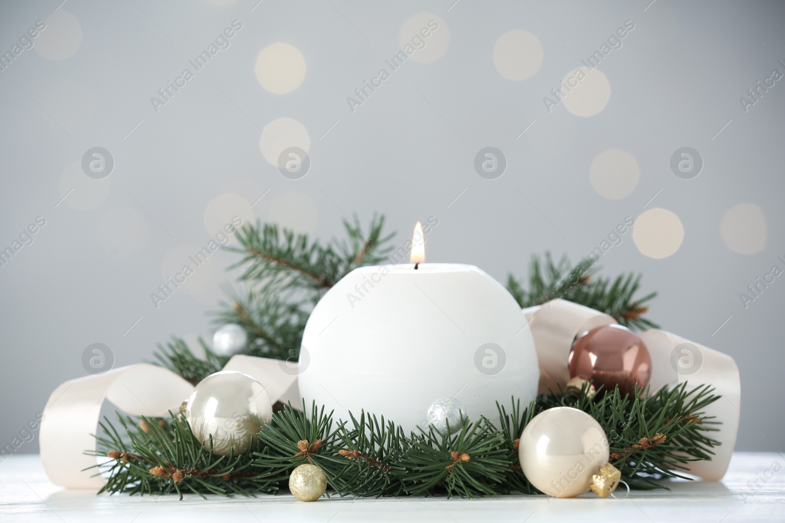 Photo of Burning white candle with Christmas decor on table against blurred lights