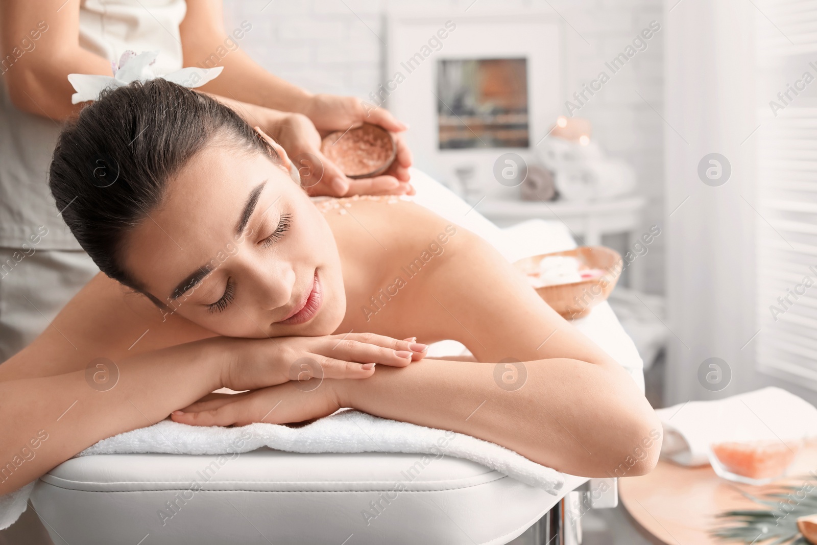 Photo of Young woman having body scrubbing procedure with sea salt in spa salon