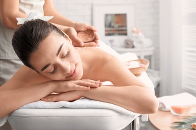 Young woman having body scrubbing procedure with sea salt in spa salon