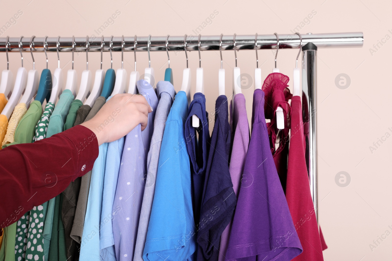 Photo of Woman choosing clothes from wardrobe rack on color background, closeup