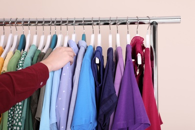 Photo of Woman choosing clothes from wardrobe rack on color background, closeup