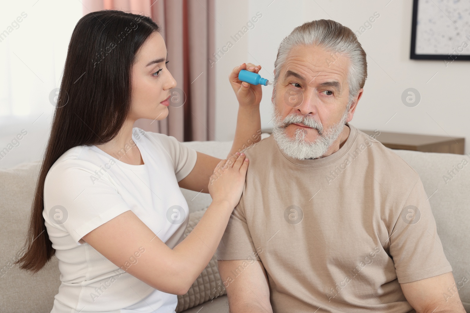 Photo of Young woman dripping medication into man's ear at home