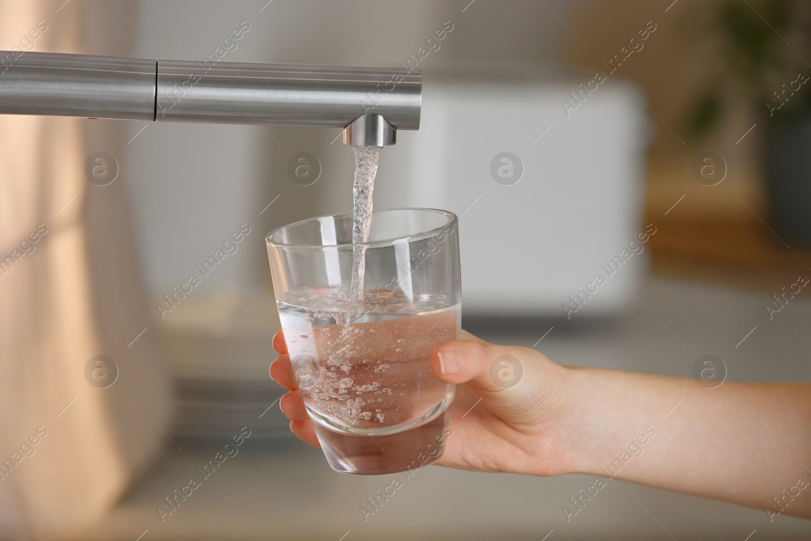 Photo of Woman filling glass with tap water from faucet in kitchen, closeup