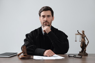 Photo of Judge with gavel and papers sitting at wooden table against light grey background