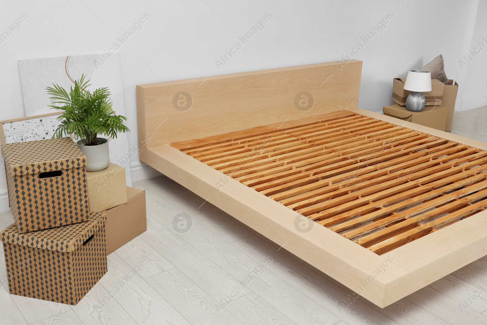 Photo of New wooden bed frame, moving boxes and decor elements indoors