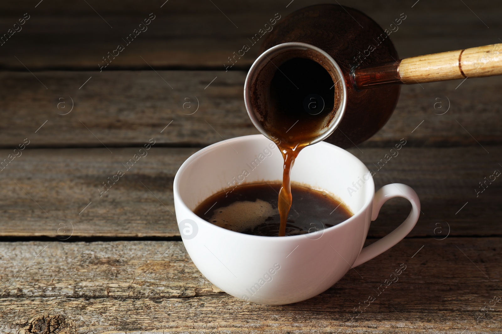 Photo of Turkish coffee. Pouring brewed beverage from cezve into cup at wooden table, closeup. Space for text