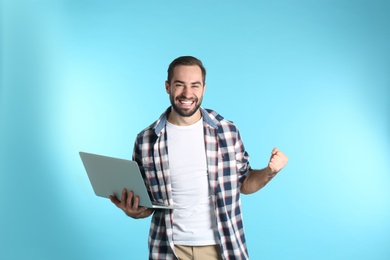 Photo of Emotional young man with laptop celebrating victory on color background