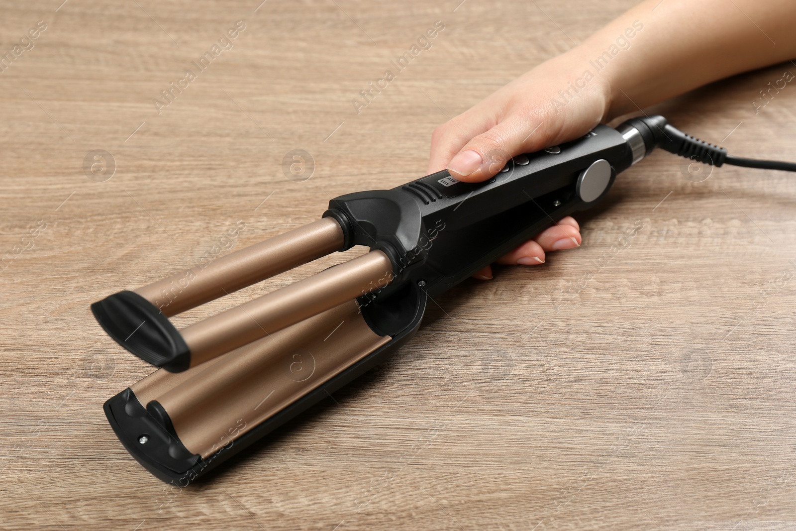 Photo of Woman holding modern triple curling iron on wooden background, closeup