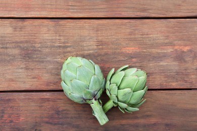 Photo of Fresh raw artichokes on wooden table, flat lay