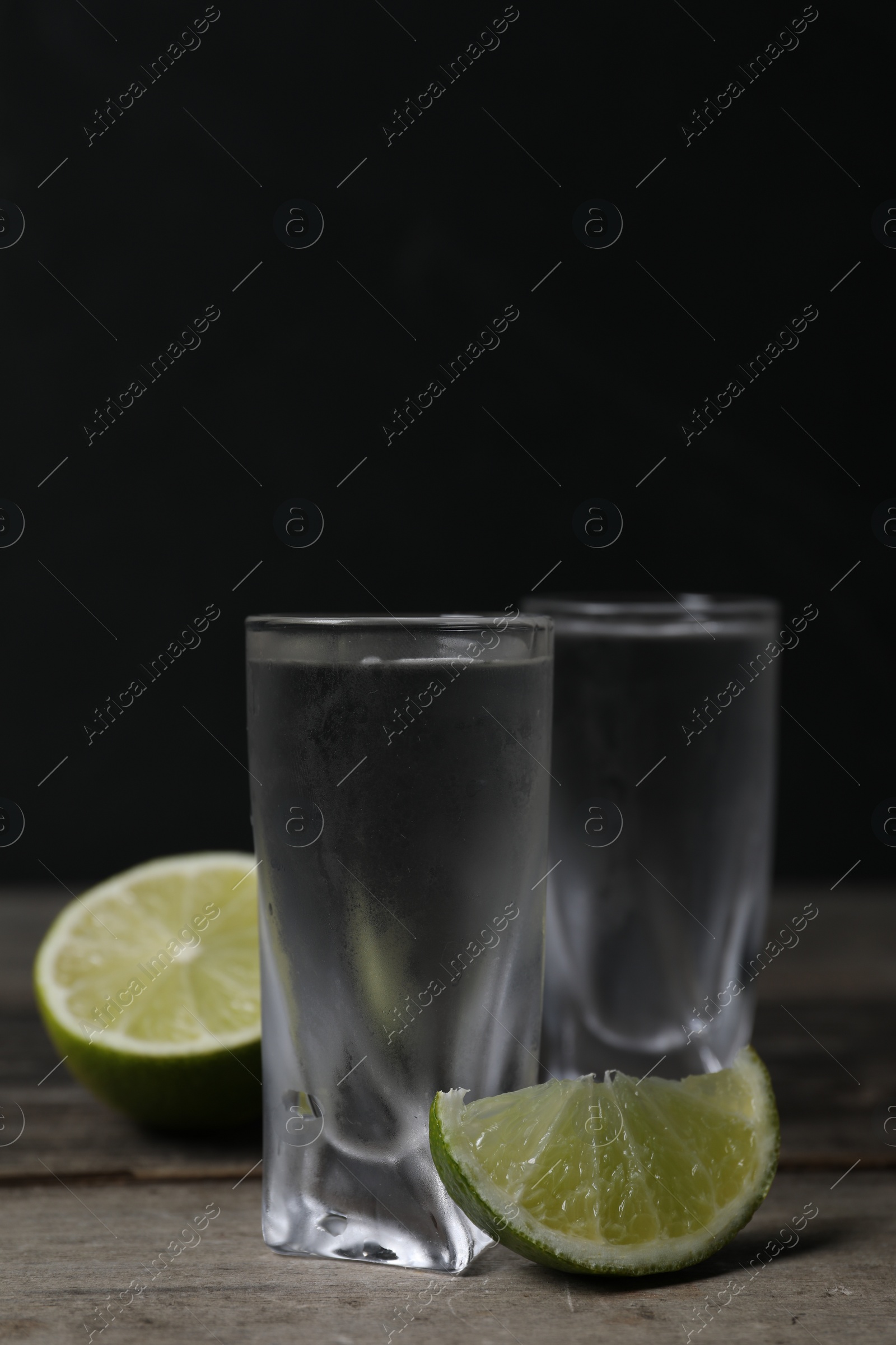 Photo of Shot glasses of vodka with lime on wooden table. Space for text